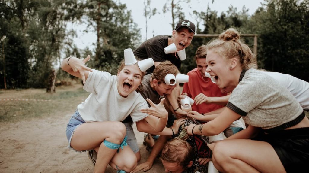 Energetic group of teenagers playing outdoors, with laughter and cups in a pile.